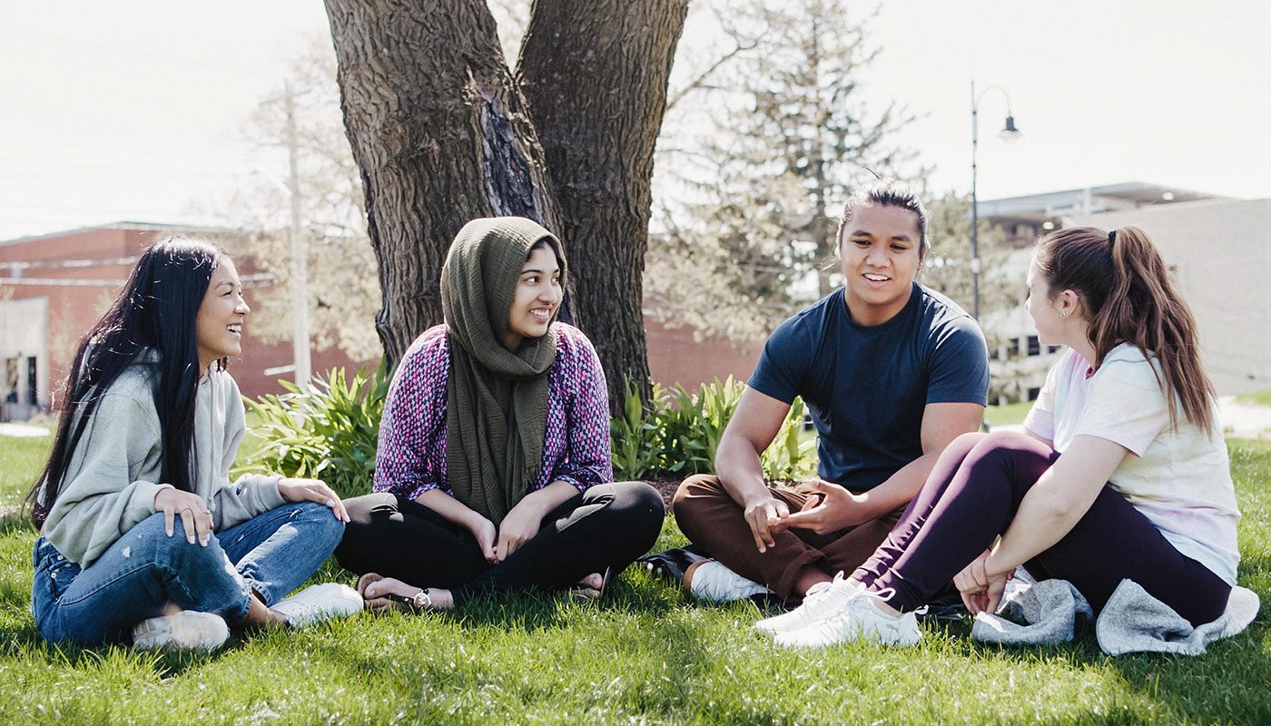 Four students sitting on the ground in front of a tree