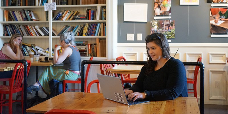 Sarah Golding sits in a colorful cafe at a table with her laptop